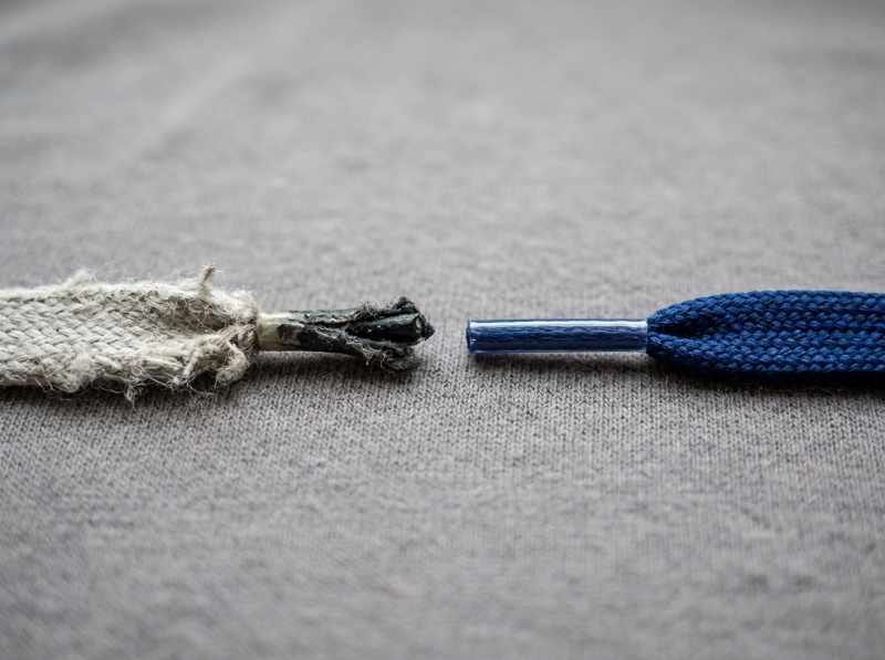 Close-up comparison of a worn-out, frayed white shoelace next to a vibrant, crisp new blue shoelace on a neutral fabric background.